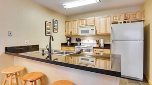 Una cocina con armarios de madera, encimera negra, refrigerador blanco y pileta de acero inoxidable.