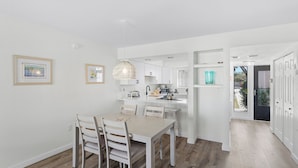 A modern kitchen with white cabinetry, a dining area with a table and chairs, and a hallway leading to a door. - A short walk to the beach and direct pool access! (Bradenton Beach)