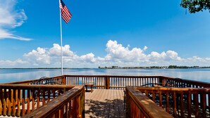 A wooden dock with a flagpole and a view of a calm body of water and distant shoreline. - A short walk to the beach and direct pool access! (Bradenton Beach)