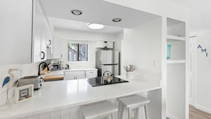 A modern kitchen with white cabinetry, a central island with stools, a built-in oven, and a refrigerator. - A short walk to the beach and direct pool access! (Bradenton Beach)