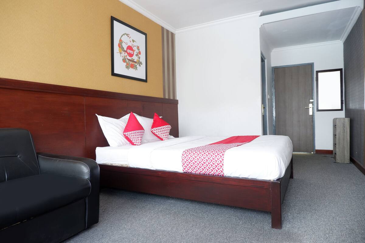 A hotel room with a wooden headboard bed, a black leather chair, and a framed picture on the wall.