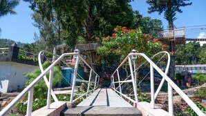 A wooden bridge with white railings leading to a platform with a view of trees and a building in the background. - Collection O 908 Taman Wisata Kopeng (Getasan)