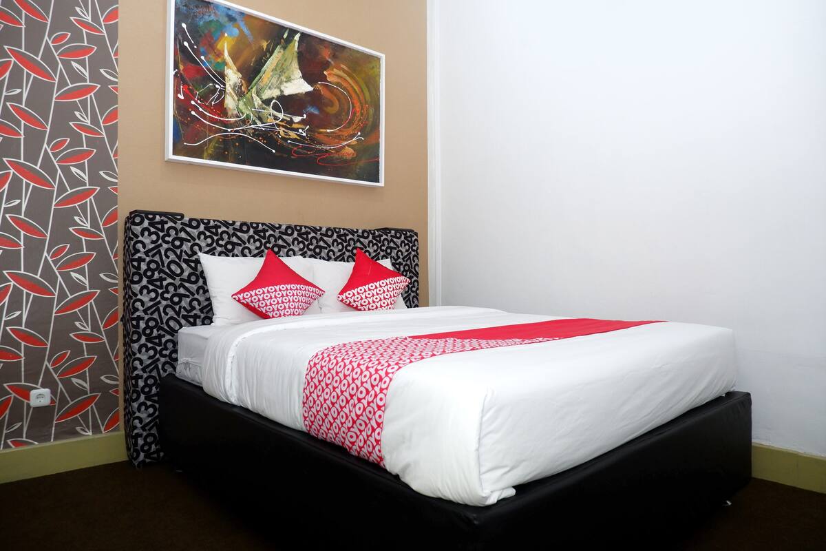 A neatly made bed with a patterned headboard, a red and white throw blanket, and matching pillows.
