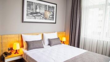Ein Hotelzimmer mit einem Bett, zwei Nachttischlampen, einem gerahmten Bild an der Wand und einem Fenster mit Vorhängen.