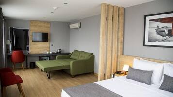 Una habitación de hotel con una cama, un sofá verde, un escritorio y un televisor.