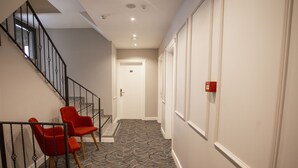 Um corredor com piso coberto por carpete, uma escada com corrimãos pretos e duas cadeiras vermelhas.