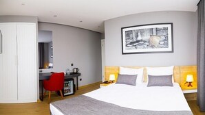 Quarto de hotel com cama, escrivaninha, cadeira vermelha, guarda-roupa branco e um quadro na parede.