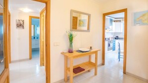 Un couloir avec une console en bois, un miroir et un vase rempli de fleurs. Des portes donnent accès à d’autres pièces.