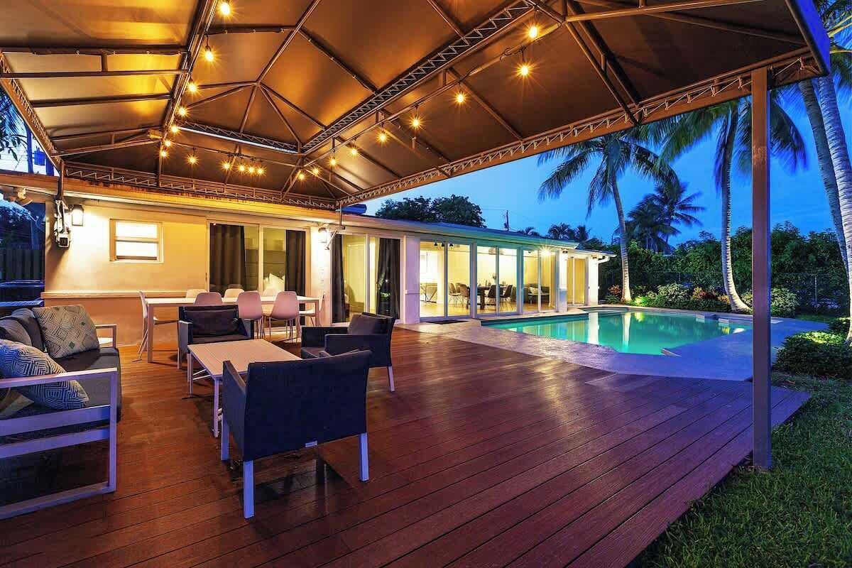 Un patio al aire libre con suelo de madera, una piscina y una zona de estar cubierta con mesas y sillas.