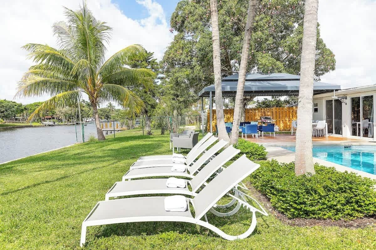 Zona de piscina con sillas de descanso, un área de estar cubierta y vista a un lago.