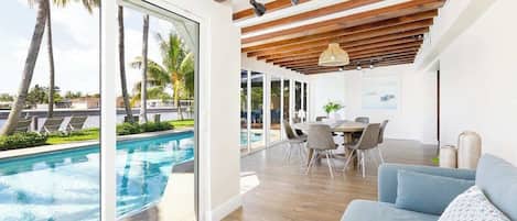 A modern living room with a pool view, wooden ceiling beams, and a dining area.