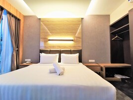 Uma cama bem arrumada com roupa de cama branca e uma toalha enrolada, um telefone de mesa e um luminário fixado na parede.