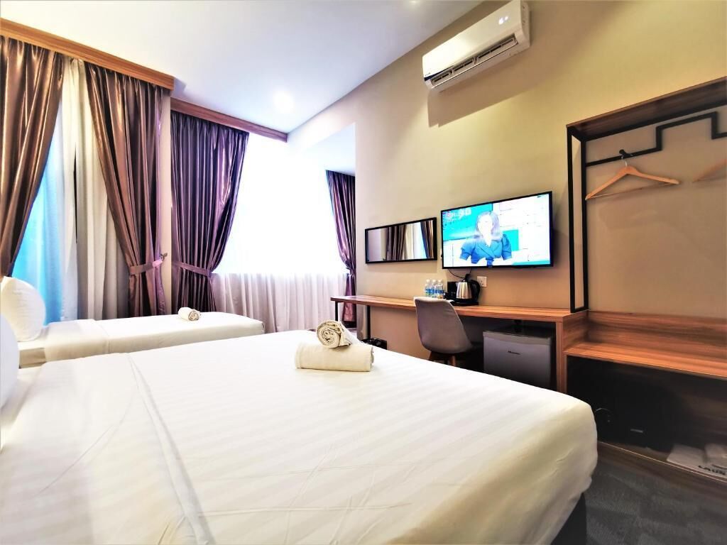 A hotel room with two beds, a desk with a computer, a TV, and a wardrobe.