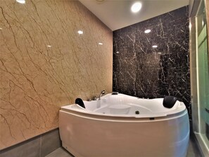 Un baño moderno con una bañera independiente, paredes de mármol e iluminación empotrada.