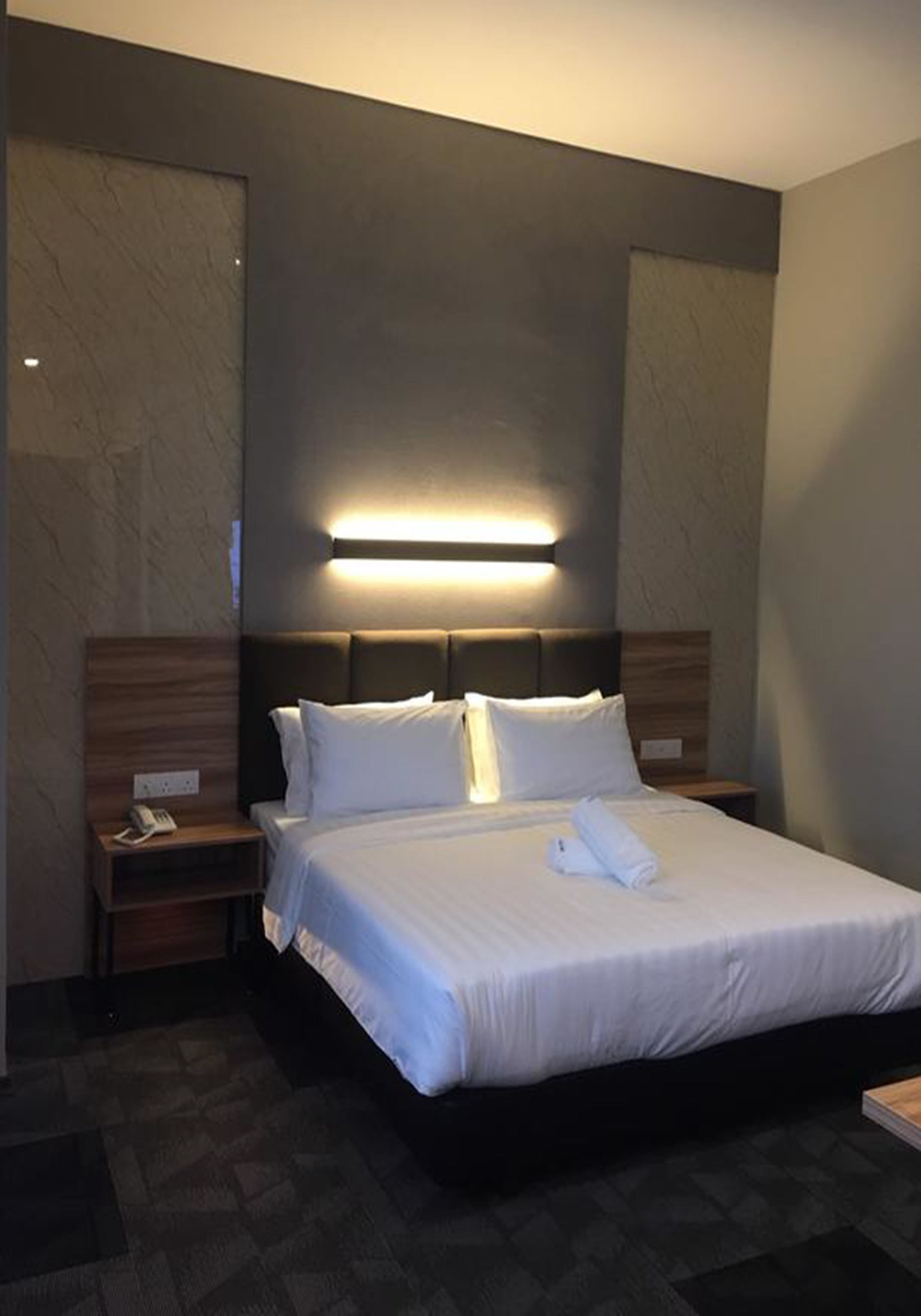Habitación de hotel con una cama grande, una mesita de noche con teléfono y una lámpara fijada a la pared.
