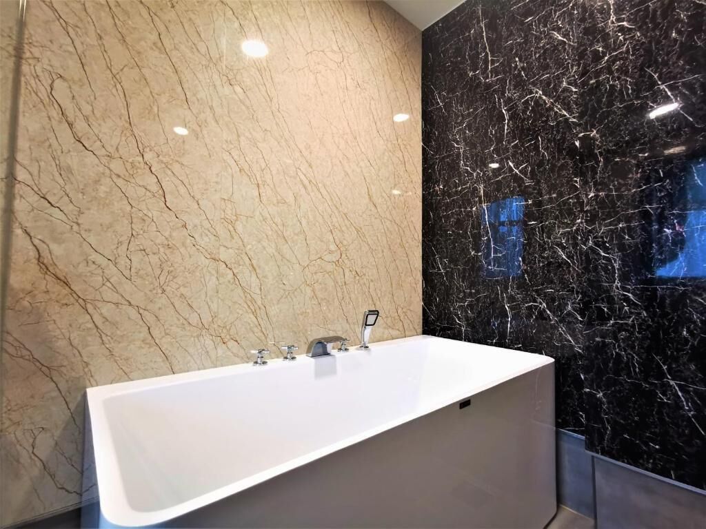 A modern bathroom with a large white bathtub, beige and black marble walls, and a sleek faucet.