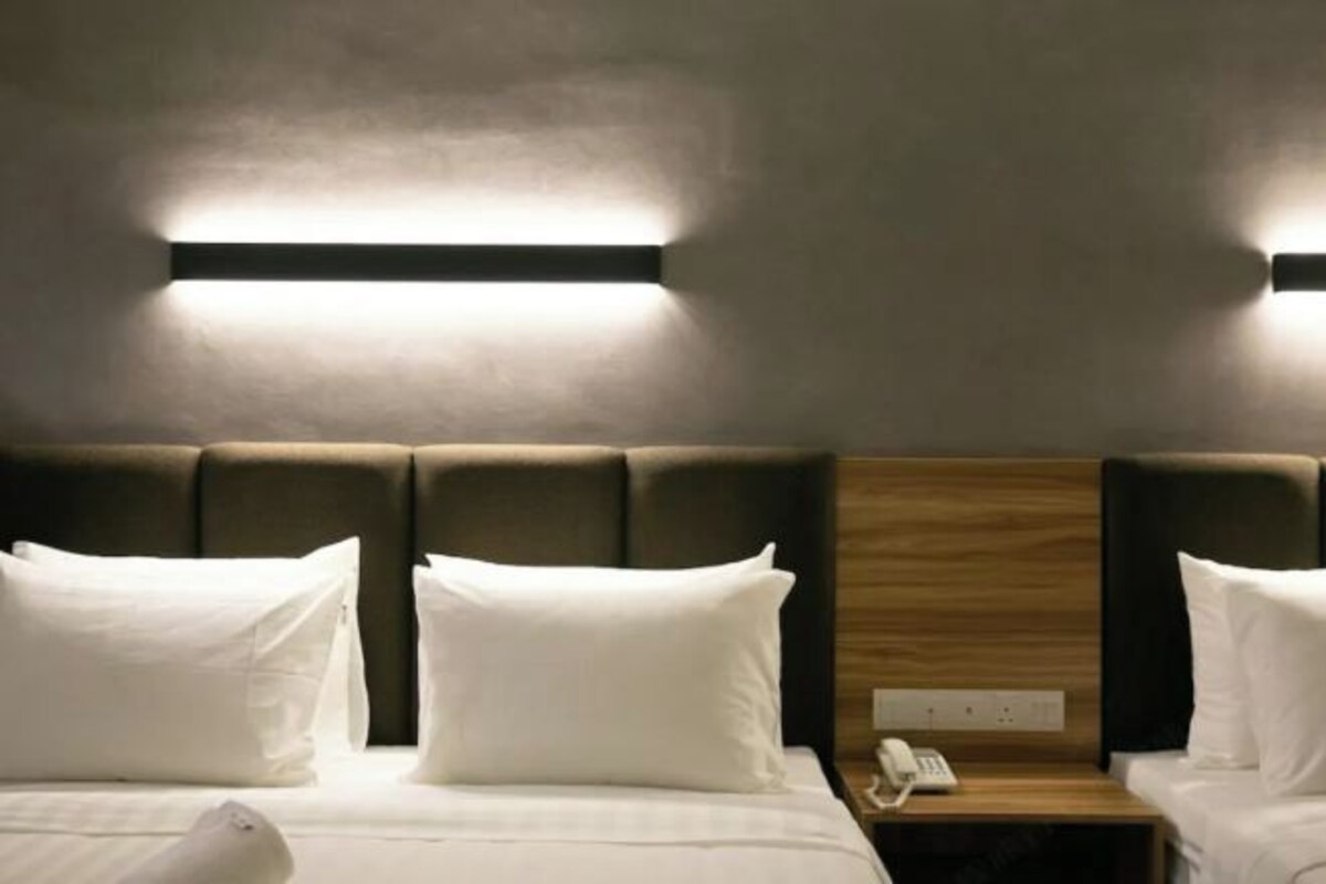 A hotel room with a bed, two bedside tables, a nightstand, and a wall-mounted light fixture.