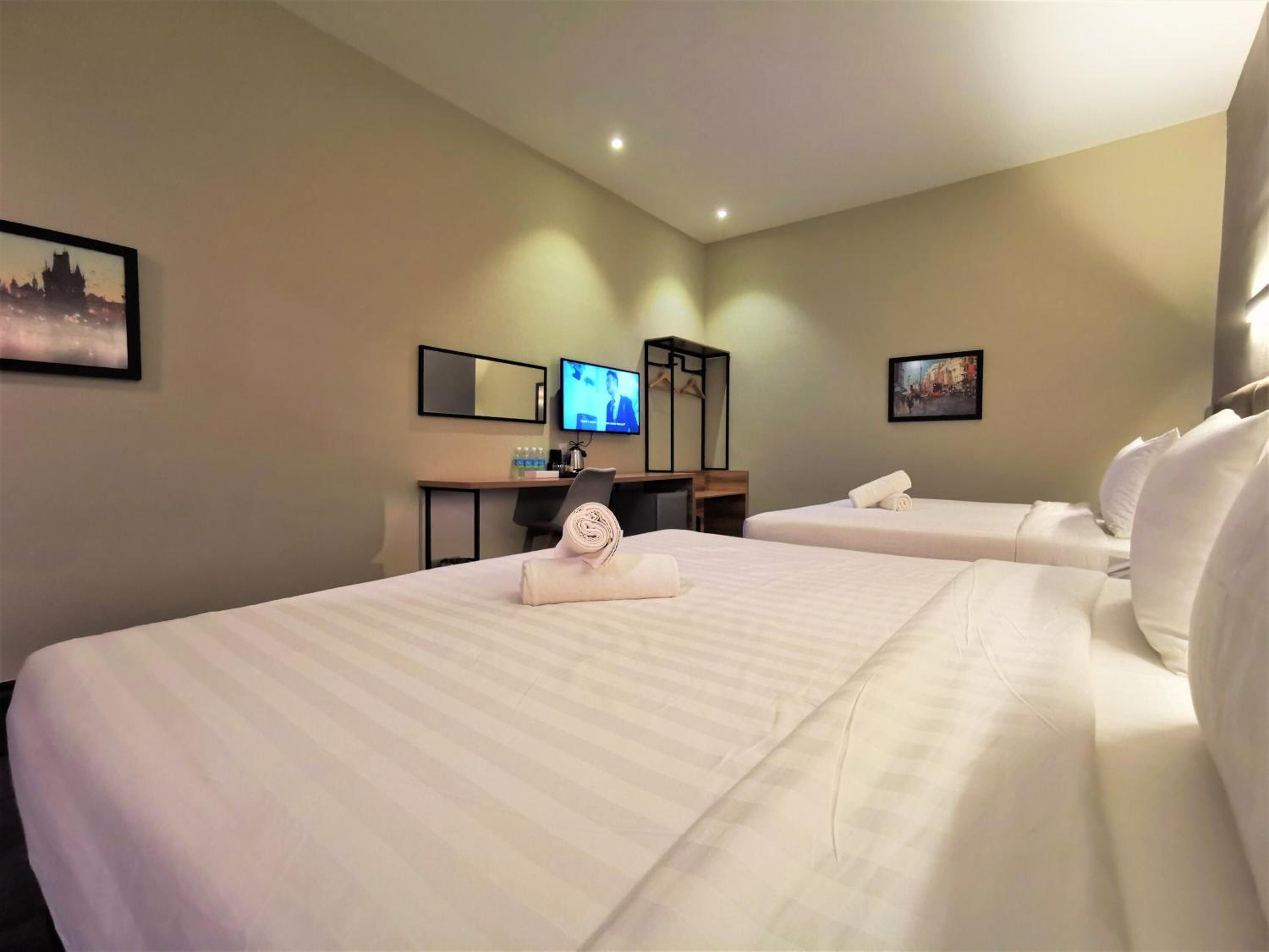 A hotel room with two beds, a desk with a computer, a television, and artwork on the walls.