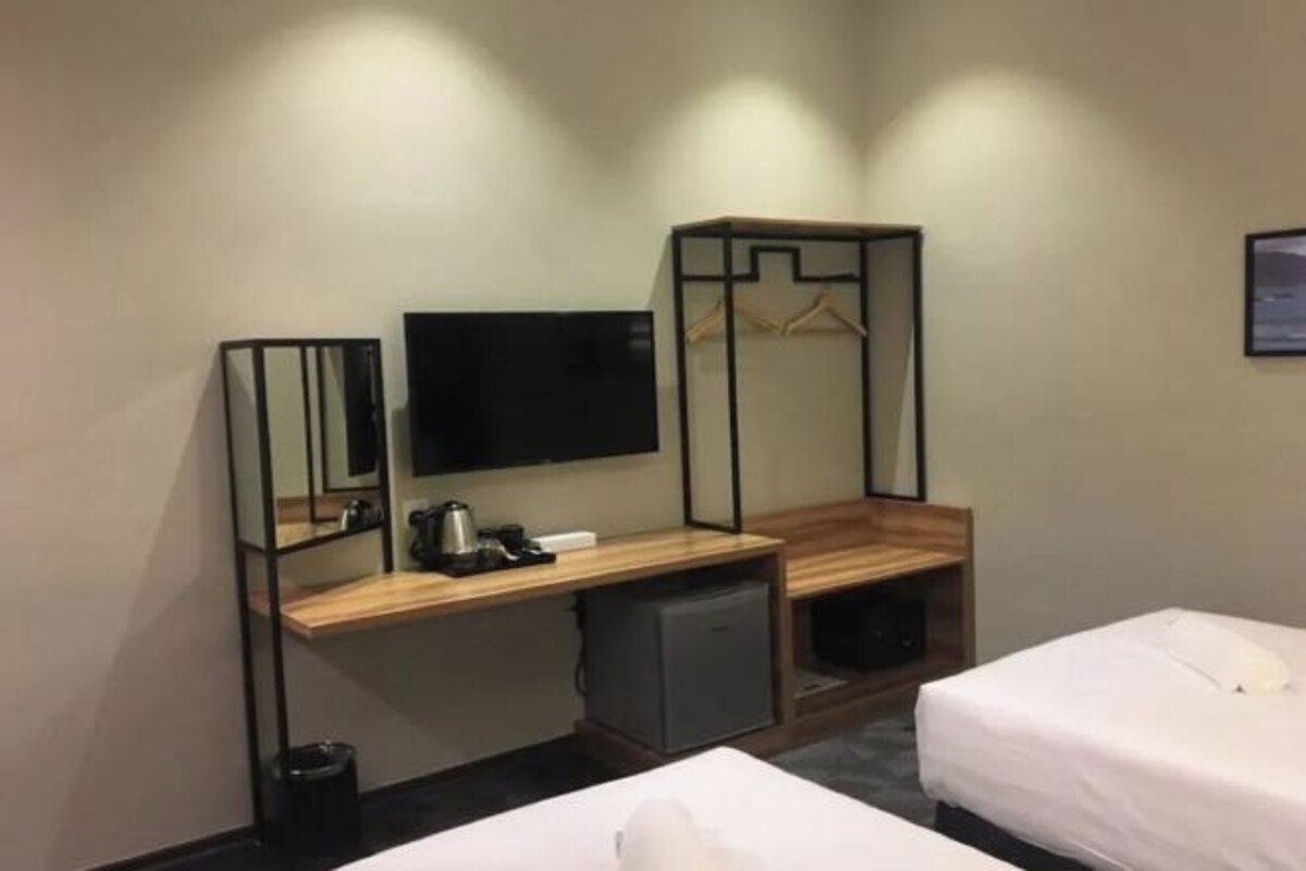 A hotel room with a wooden desk, a television, a small refrigerator, two beds, and a wall-mounted TV.