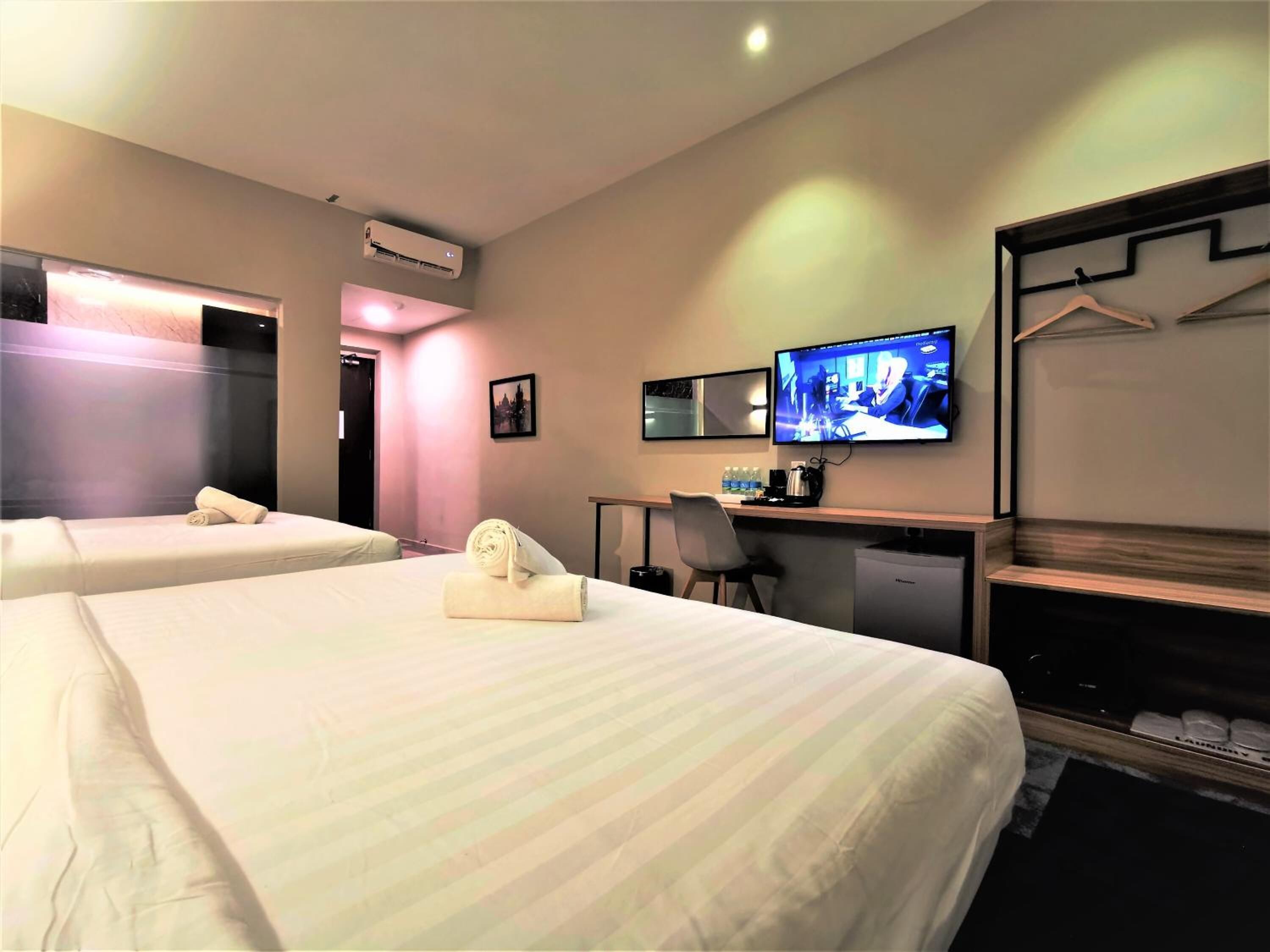 A hotel room with two beds, a desk with a computer, a television, and a wardrobe.