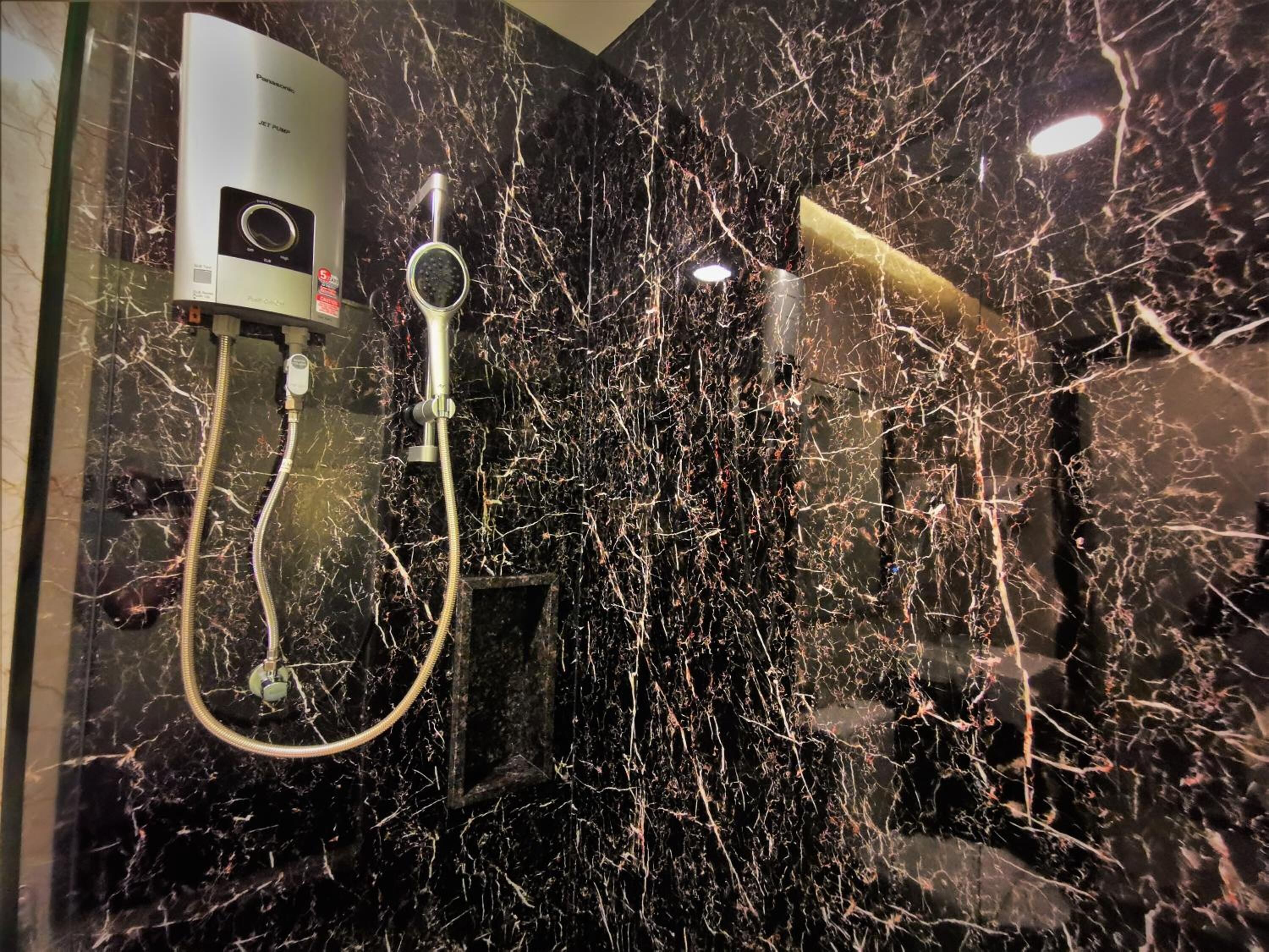 A bathroom with a black marble wall, a handheld showerhead, and a wall-mounted faucet.