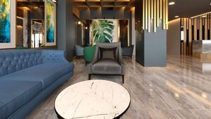 A modern lobby with a blue sofa, a round marble coffee table, and a large plant in the center. - Grand Krone Hotel (Cinarcik)