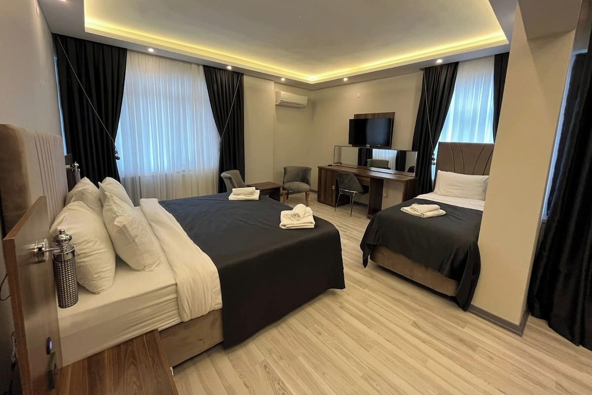 A hotel room with two beds, a desk, a TV, and a shower.