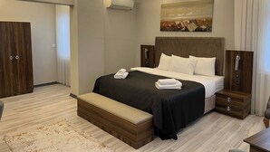 A modern bedroom with a large bed, bedside tables, a bench, an air conditioning unit, and a painting on the wall. - Grand Krone Hotel (Cinarcik)