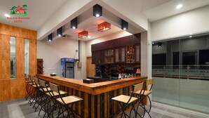 A modern bar area with a wooden bar counter and black metal chairs. There are overhead lights and a refrigerator in the background. - Kalaw Garden Hotel (Kalaw)