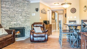 A living room with a stone fireplace, leather armchair, wooden dining table, and a bear head decoration. - Downtown Gem 💎 -102- Walk to Coffee ☕️ & Anakeesta (Gatlinburg)