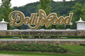 A large sign for Dolly Wood with a stone wall and flower beds in front. - Downtown Gem 💎 -102- Walk to Coffee ☕️ & Anakeesta (Gatlinburg)