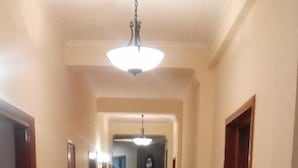 A long, narrow hallway with wooden floors and walls, leading to a room with a large window and a ceiling light.