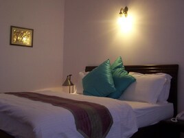 Una cama bien hecha con sábanas blancas y almohadas turquesa, una lámpara de noche y un cuadro en la pared.