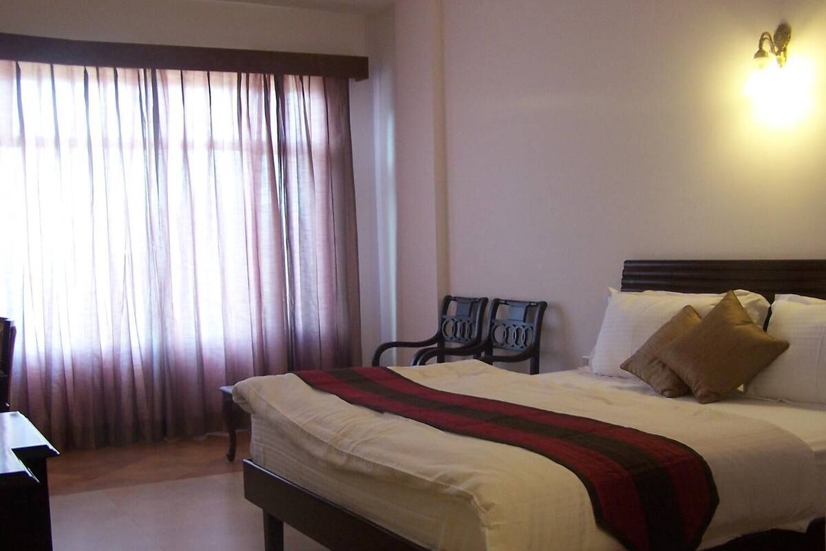 A hotel room with a bed, a desk, a chair, and a window with curtains.