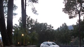 A white car parked in a parking area with stone walls and trees.