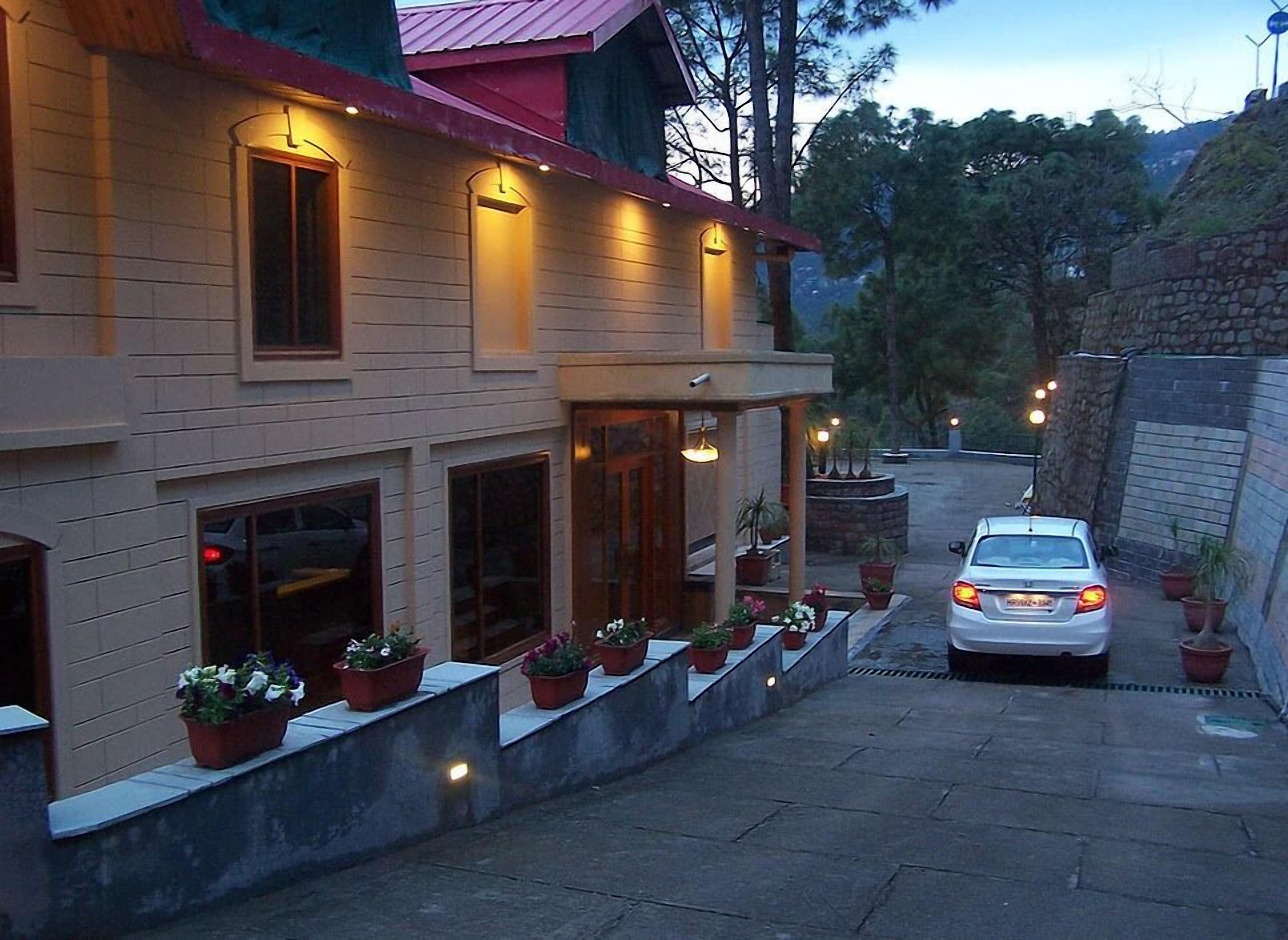 Un edificio de dos pisos con techo rojo, un porche cubierto con plantas en macetas y un coche estacionado en la entrada.