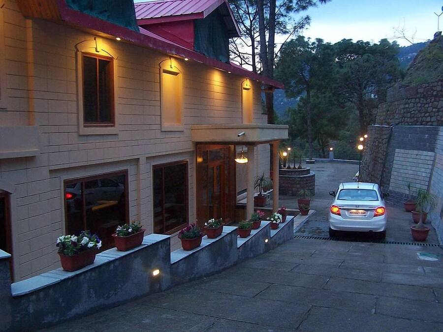 Un edificio de dos pisos con techo rojo, un porche cubierto con plantas en macetas y un coche estacionado en la entrada.