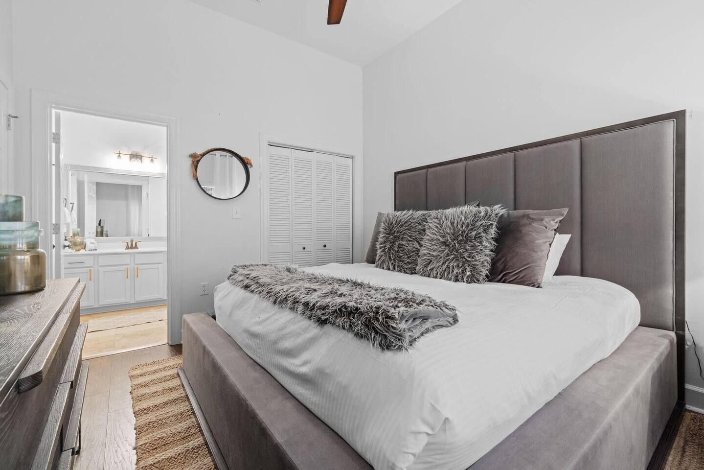 Un dormitorio moderno con una cama grande, una mesita de noche de madera, un espejo y vistas al baño.