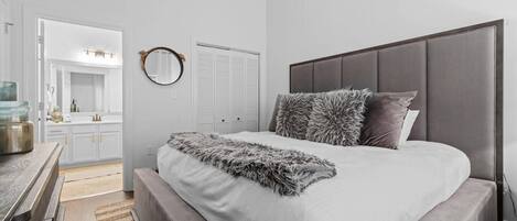 Un dormitorio moderno con una cama grande, una mesita de noche de madera, un espejo y vistas al baño.