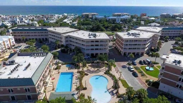 A hotel complex with multiple buildings, a central swimming pool, and a view of the ocean. - The Newcastle Updated 3BR/2BA ~ Best Location! (Inlet Beach)