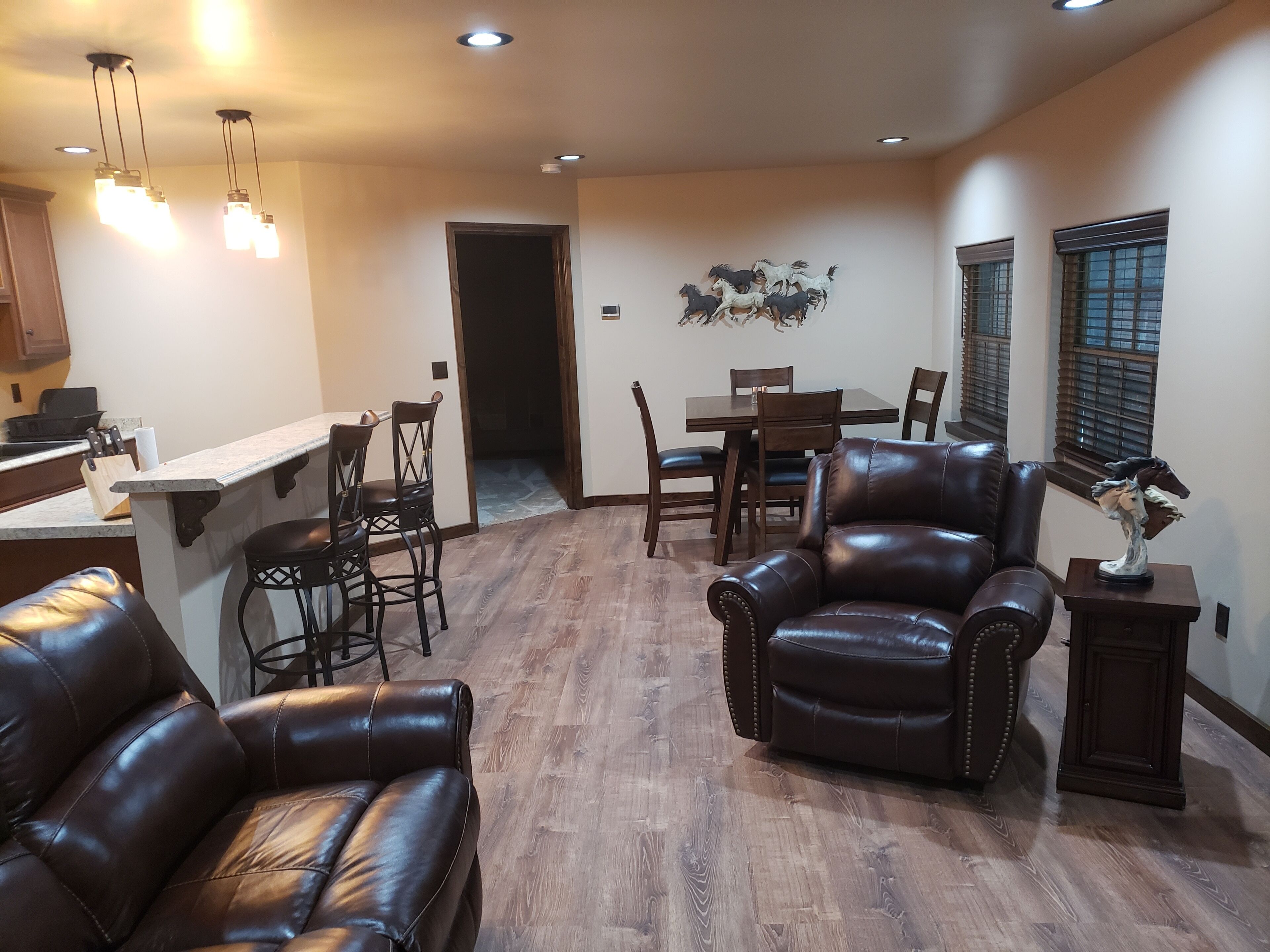 A spacious living area with leather sofas, a dining table, and chairs. There is a kitchen area with a countertop and cabinets.