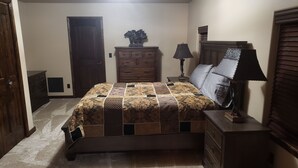 A bedroom with a bed, dresser, nightstand, lamp, and a door.