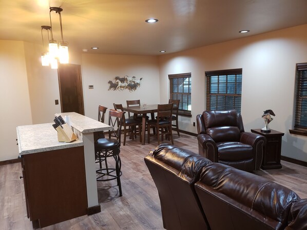 A spacious living area with a dining table, leather sofa, and a kitchen island with a knife block.