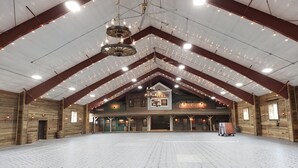 A spacious indoor venue with high ceilings, exposed wooden beams, and a central chandelier.