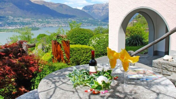 A table with a bottle of wine, a glass, and a decorative item, set against a scenic mountain backdrop.