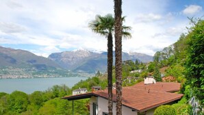 A house with a red roof, surrounded by lush greenery and a mountain backdrop.