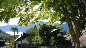 A park with a playground, benches, and a view of mountains and a lake.
