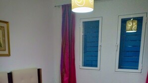 Un dormitorio con cama, ventana con persianas azules y lámpara colgante.