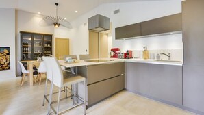 A modern kitchen with a central island, built-in appliances, and a dining area with white chairs.