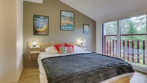 A bedroom with a bed, a nightstand, and a window with a view of greenery.